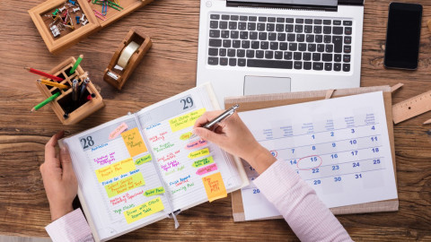 Afbeelding van een jongen/meisje ide aan het plannen is in ene planner en een laptop die erachter 