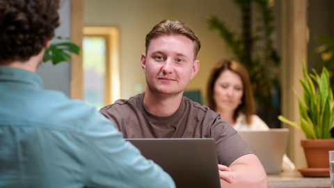 Twee mensen werken op laptops in een moderne kantoorruimte met groene planten.