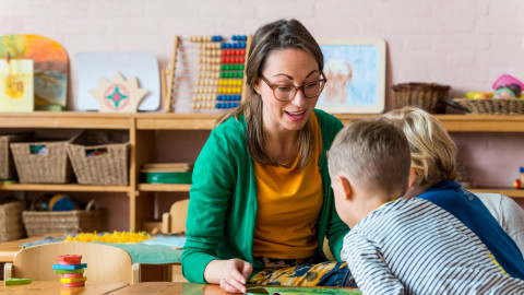 Twee kinderen lezen samen een boek aan een tafel in een kleurrijke klasruimte.