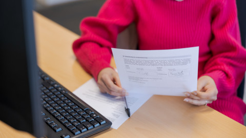 Persoon in roze trui leest een document aan een bureau met toetsenbord.