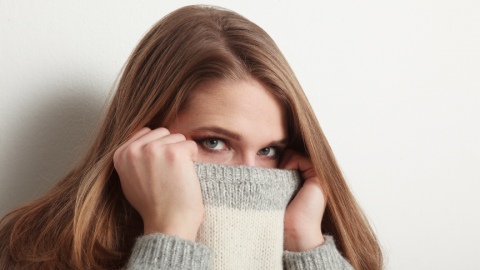 Vrouw met lang bruin haar, grijsgroene trui, tegen witte achtergrond.