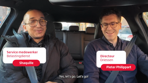 Twee personen met veiligheidsgordels in een auto, zittend op de voorstoelen.