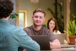 Twee mensen werken op laptops in een moderne kantoorruimte met groene planten.