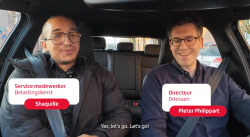 Twee personen met veiligheidsgordels in een auto, zittend op de voorstoelen.