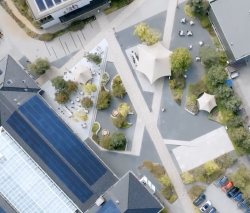 Luchtfoto van een moderne buitenruimte met gebouwen, bomen, wandelpaden en overdekte zitplaatsen.