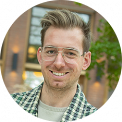 Man met blond haar, gekleed in een geruit overhemd, buiten met bakstenen en groen op de achtergrond.