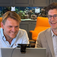 Twee mannen zitten aan een bureau met een laptop, omringd door een moderne inrichting.