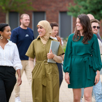 Groep mensen loopt lachend buiten op een zonnige dag, diverse kledingstijl.