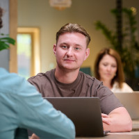 Twee mensen werken op laptops in een moderne kantoorruimte met groene planten.