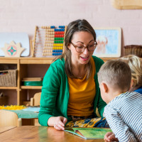 Twee kinderen lezen samen een boek aan een tafel in een kleurrijke klasruimte.