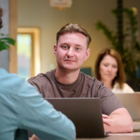 Man achter laptop in een moderne kantoorruimte met planten en laptops op de achtergrond.