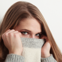 Vrouw met lang bruin haar, grijsgroene trui, tegen witte achtergrond.