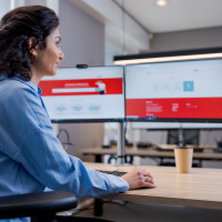 Vrouw aan bureau kijkt naar computerscherm met rood-witte interface in een modern kantoor.